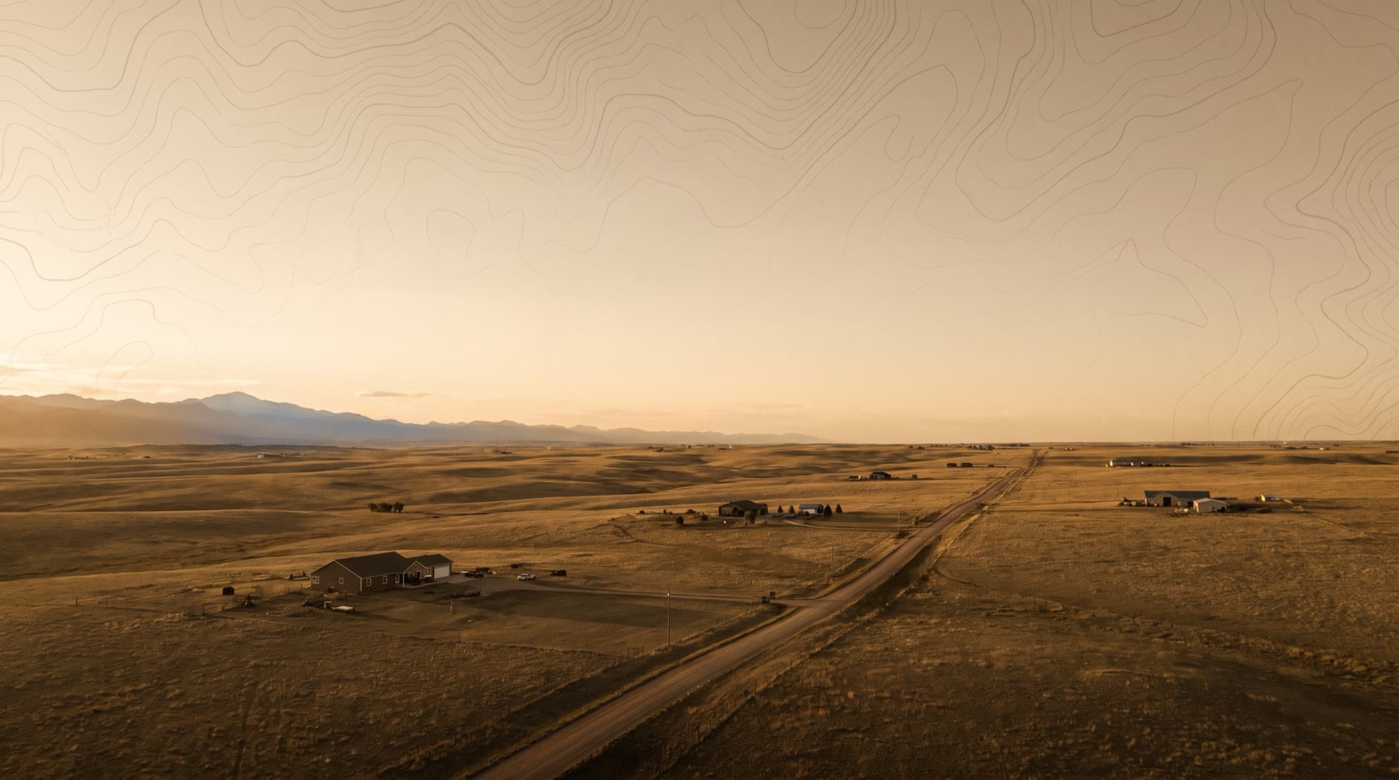 Rolling high-plains prairie with scattered rural homes and a road running to the distant Front Range near Falcon, Colorado at dusk
