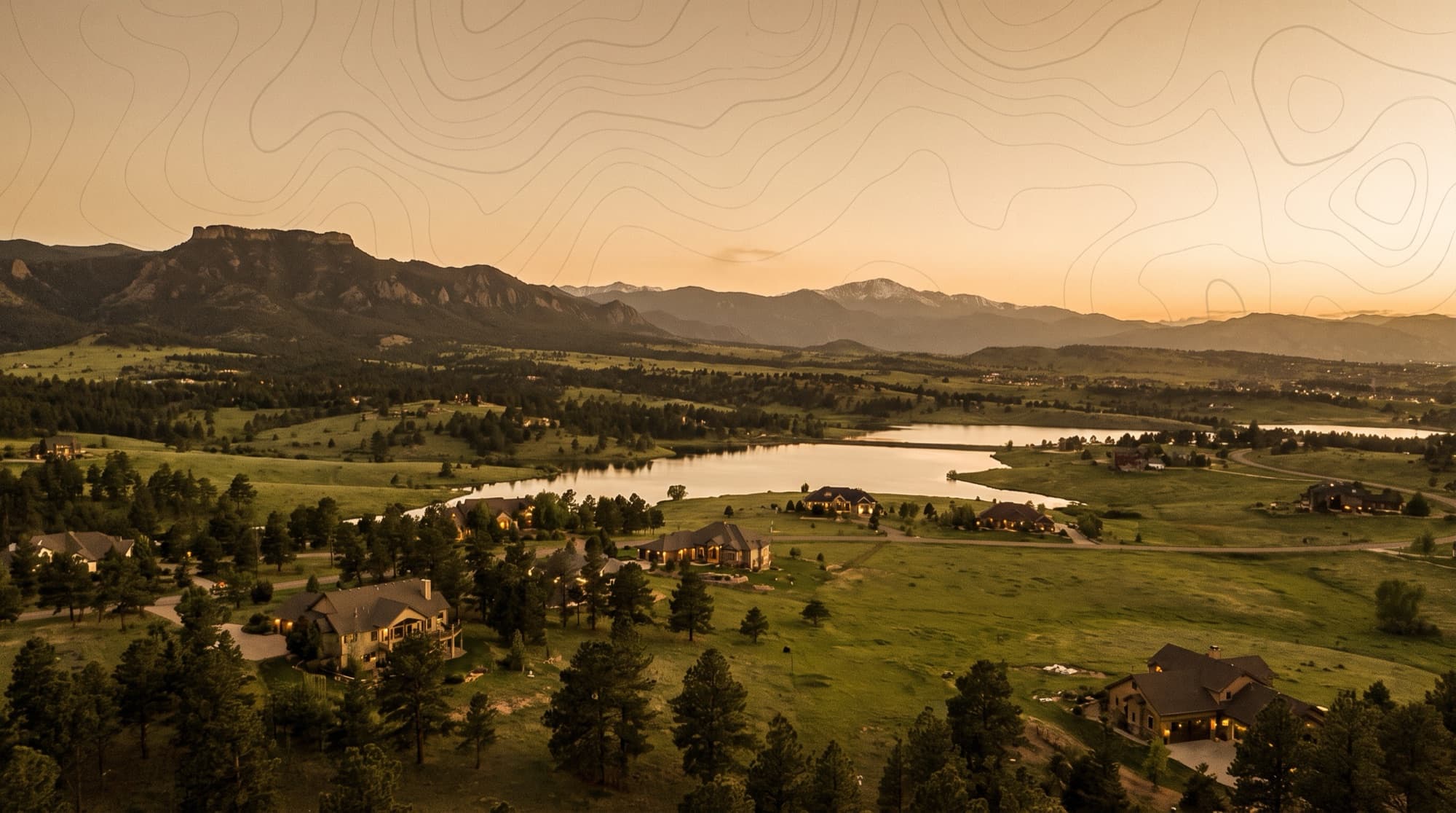 Rolling green foothills, a reservoir, and upscale homes below the northern Front Range near Monument, Colorado at dusk