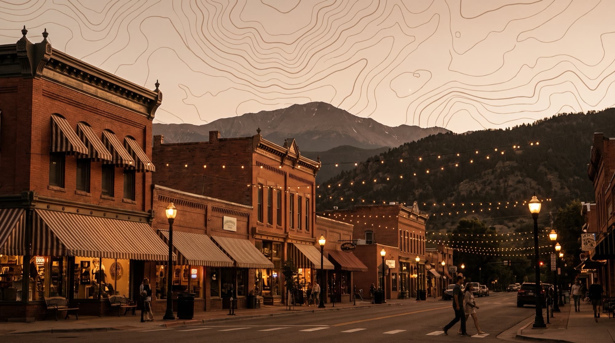 Historic red-brick storefronts and string lights along Colorado Avenue in Old Colorado City, with Pikes Peak behind at dusk