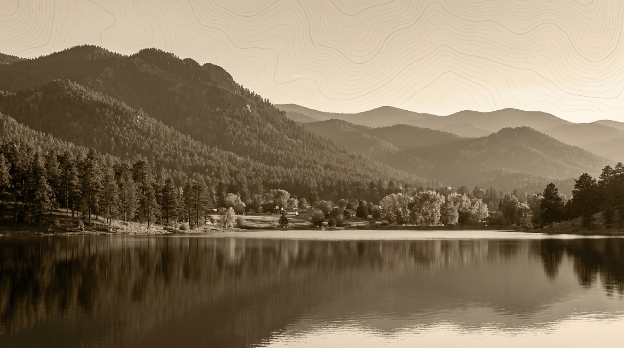 The still reservoir at Palmer Lake, Colorado reflecting pine-covered Front Range foothills and a small lakeside village at dusk